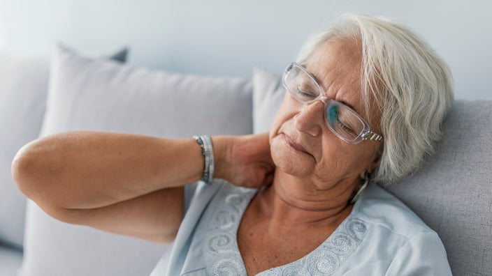 An older woman is holding her neck and appears to be in pain