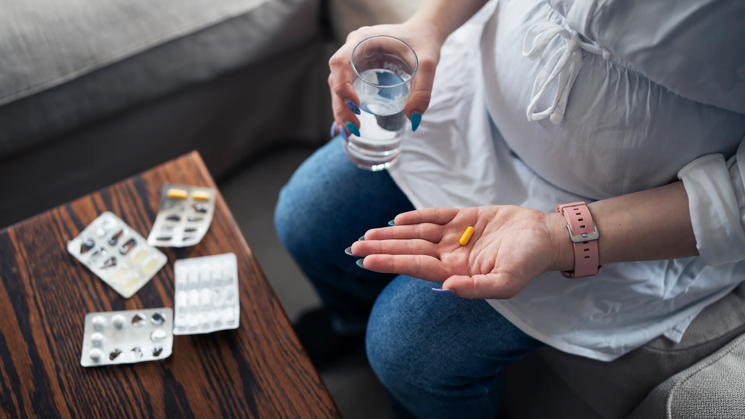 Cropped shot of a pregnant woman taking medication. She has a glass of water in one hand.