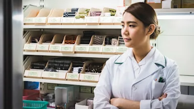 HCP Pharmacists: pharmacist arms crossed by shelf-1159790418