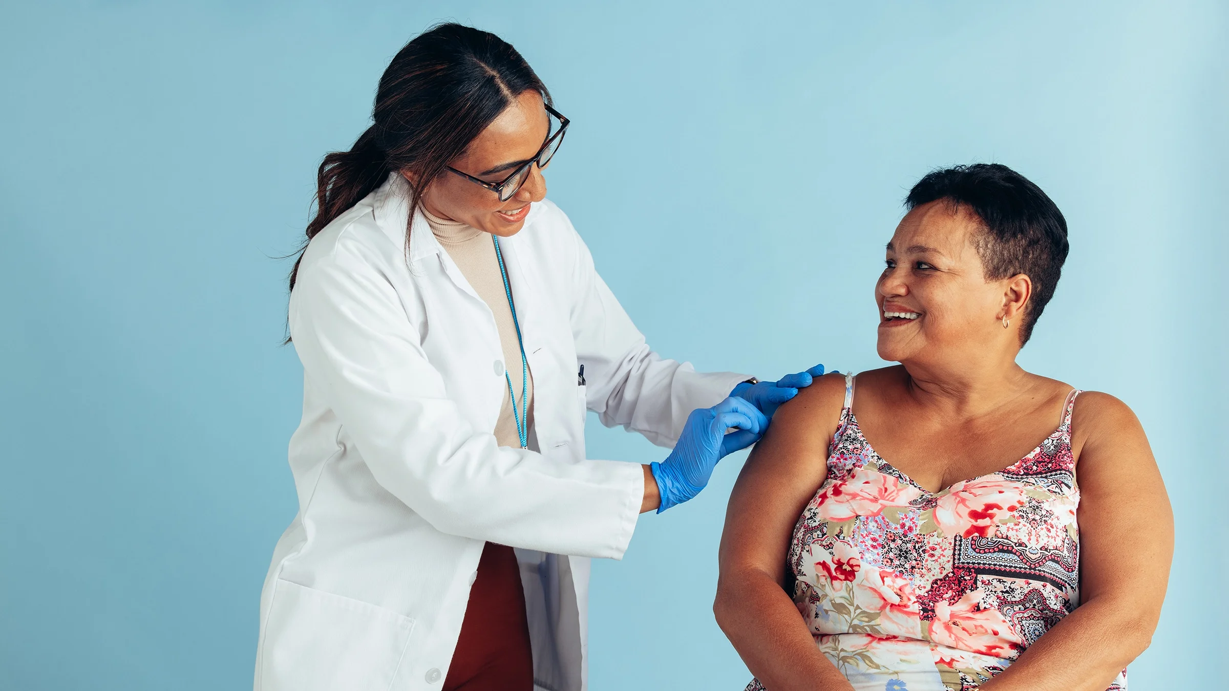 Doctor giving a woman a shot on a blue studio background.
