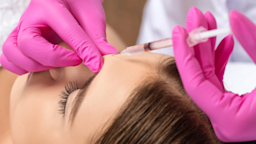 Close-up of a woman getting botox between her eyes. The person administering the injection is wearing pink gloves. 
dimid_86/iStock via Getty Images