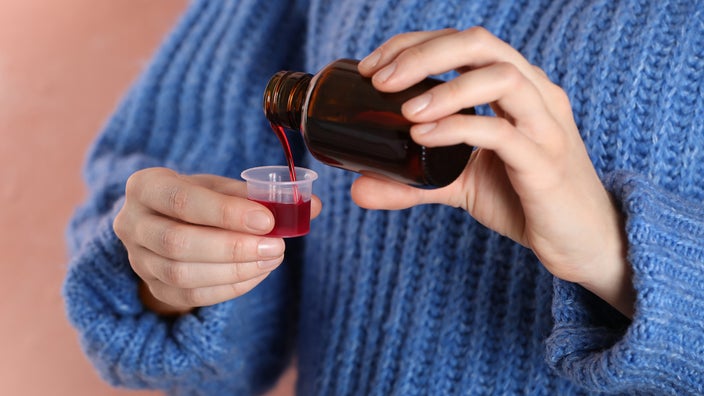 A person measures out a dose of cough medicine into a cup.