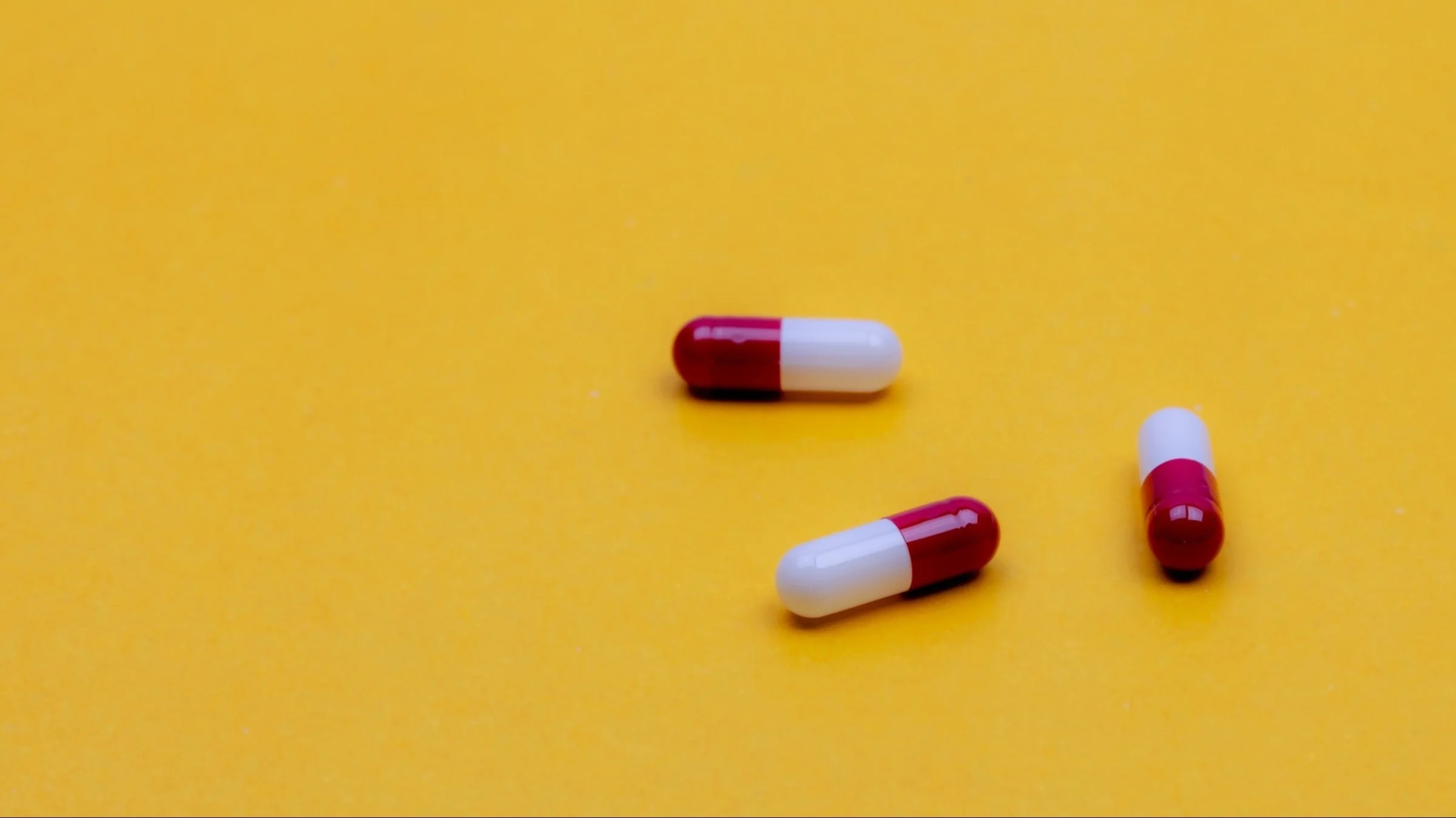 Three white and red capsule pills on a yellow background.