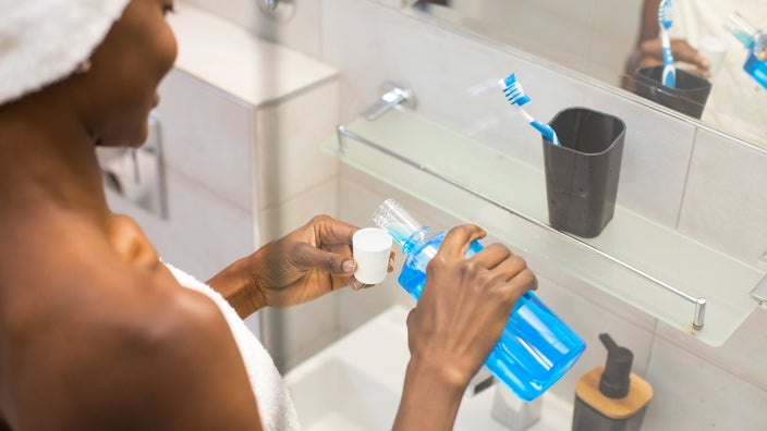 A woman pours mouthwash into a cap. 