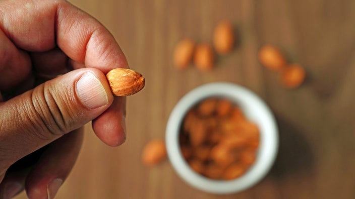 Close-up hand holding an almond with blurred bowl of almonds in the background