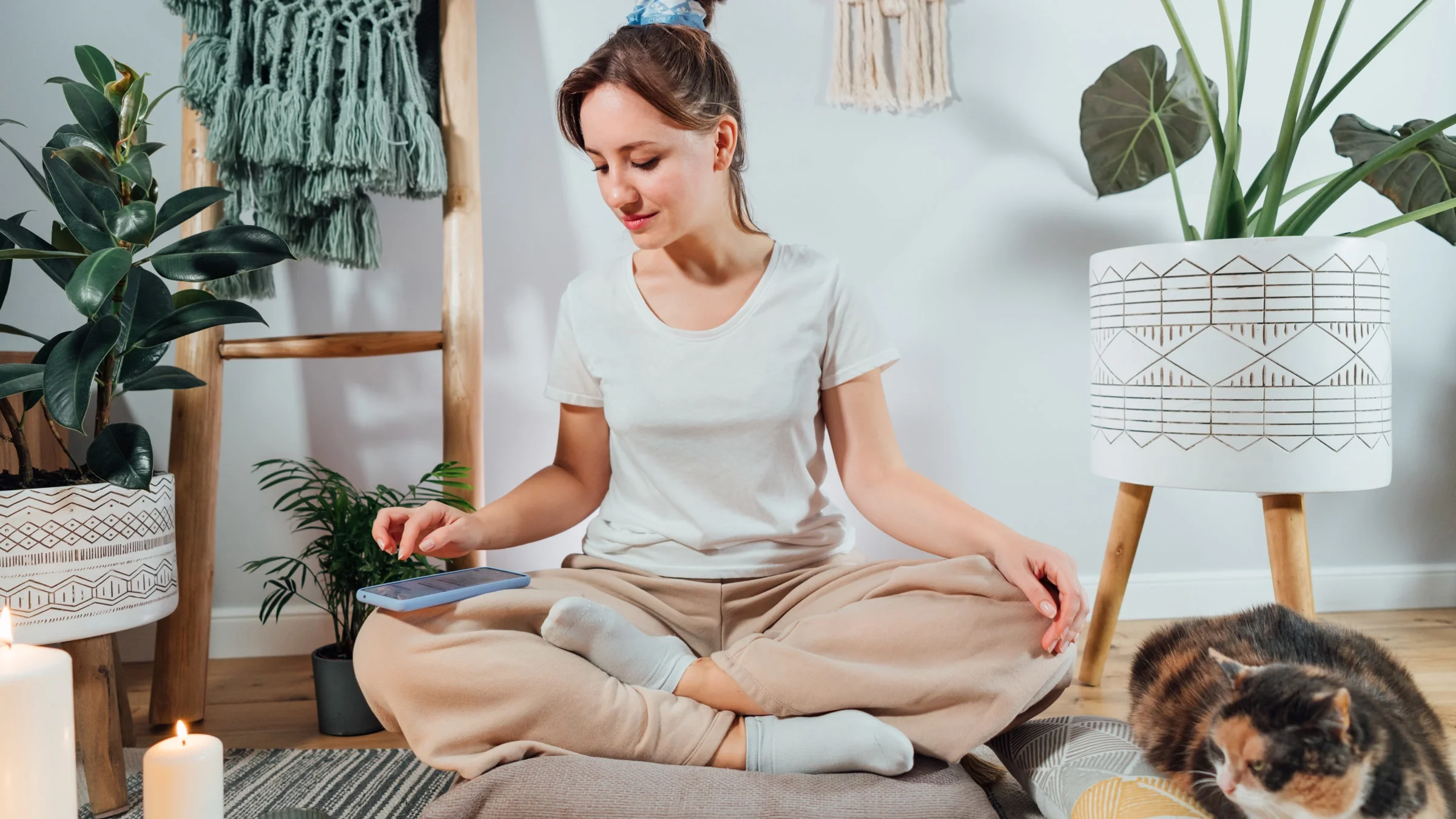 A person using their phone as they meditate next to their cat.