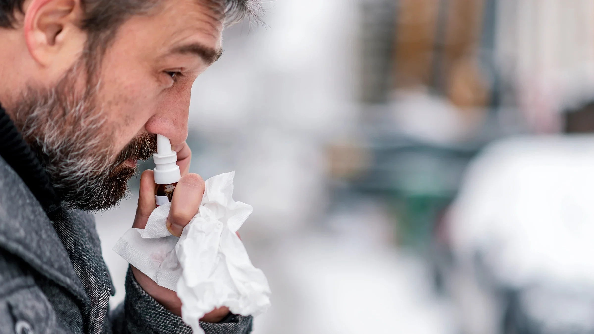 An adult is using nasal spray with tissue at hand.