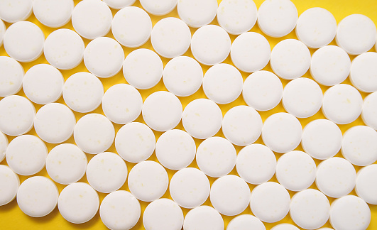 Rows of white round pills on a bright yellow background.