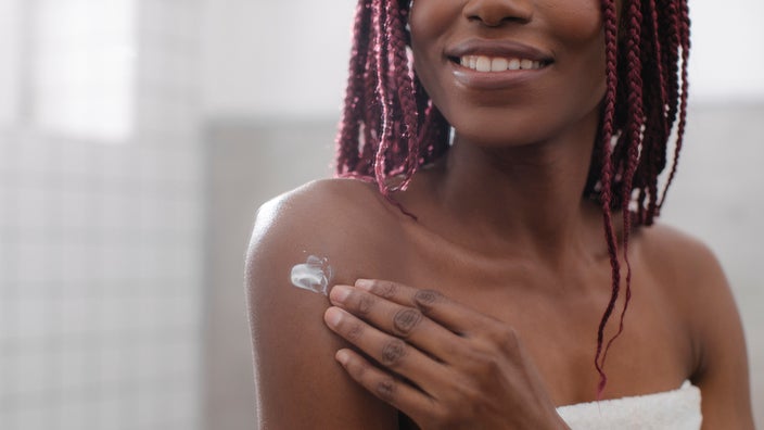 Cropped shot of a young woman applying cream to her arms and shoulder.