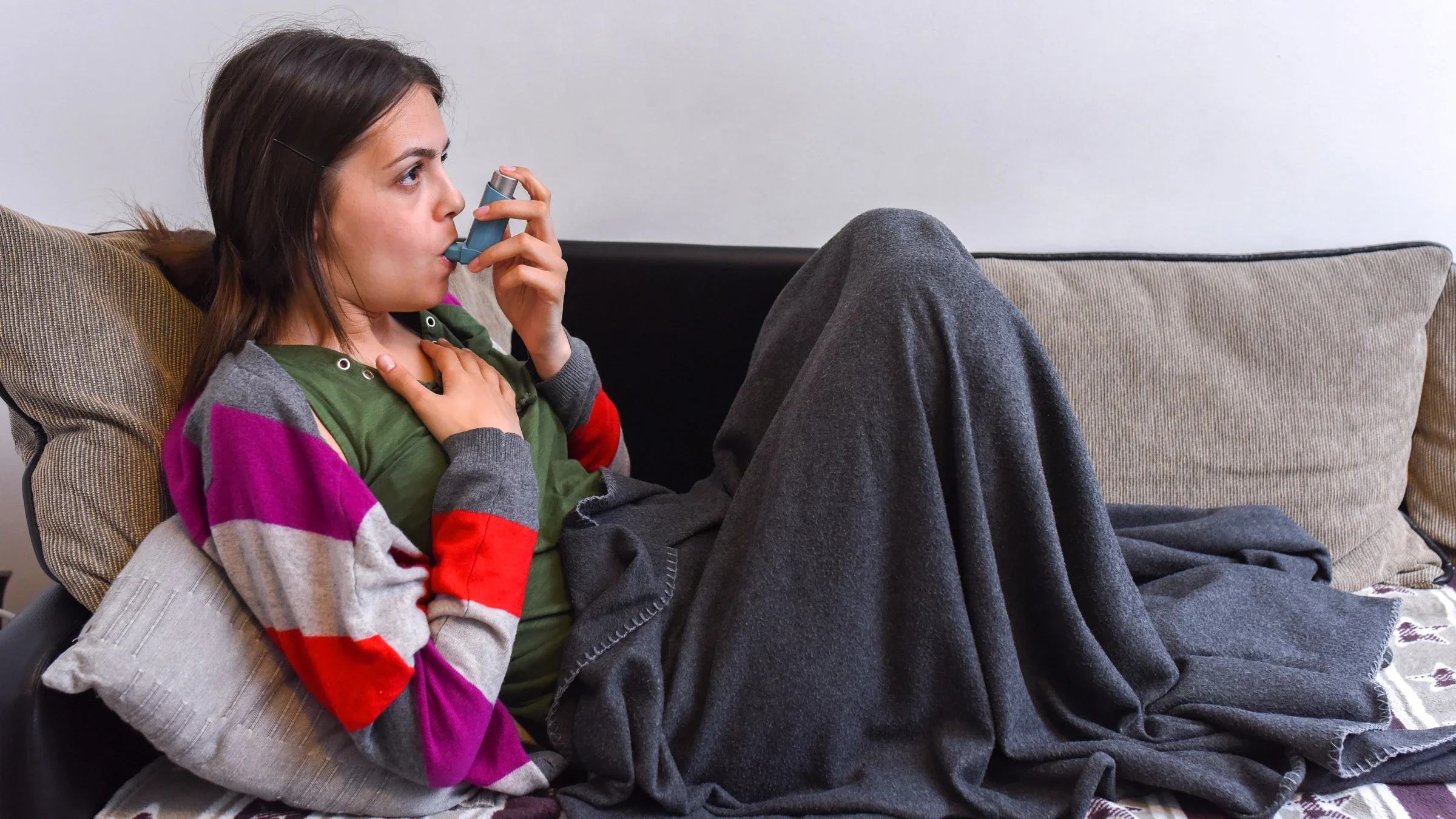 A person using an inhaler on their couch.