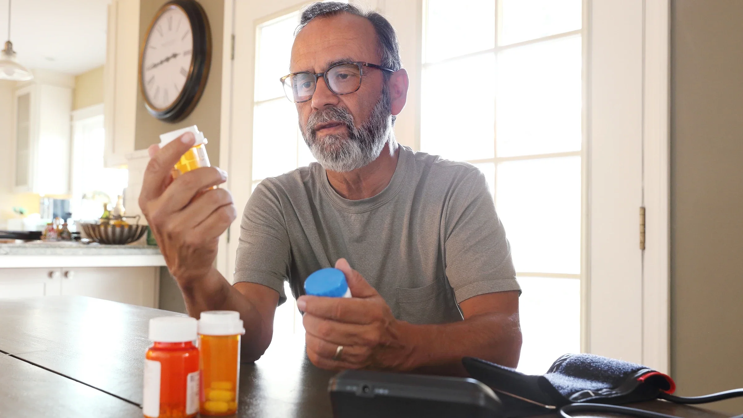 A man, with a blood pressure monitor, sorts through prescription medications.