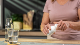 A person opening a pill bottle in their kitchen, next to water.
simonkr/E+ via Getty Images  
