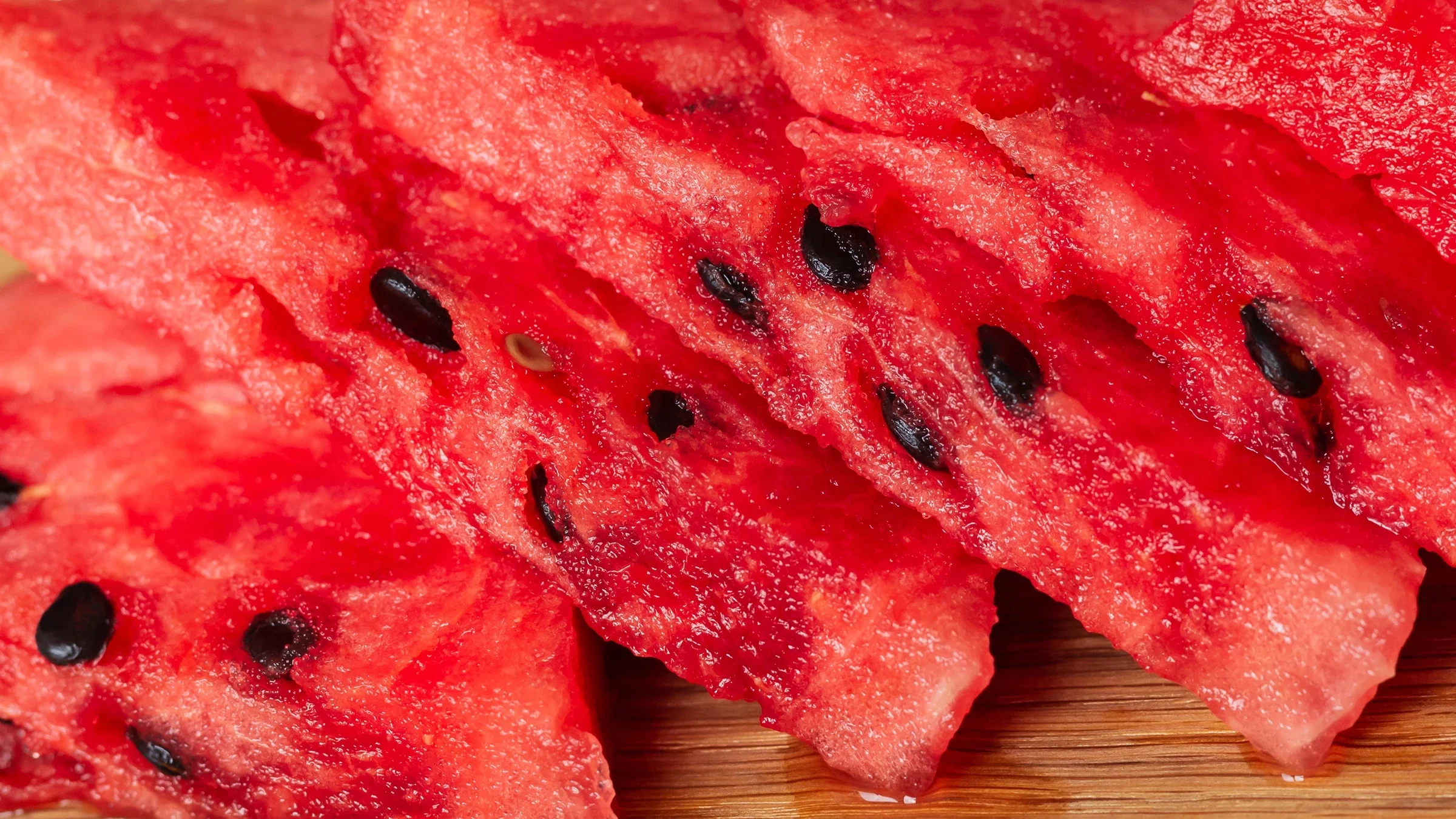 Triangular slices of watermelon lie on a wooden surface.