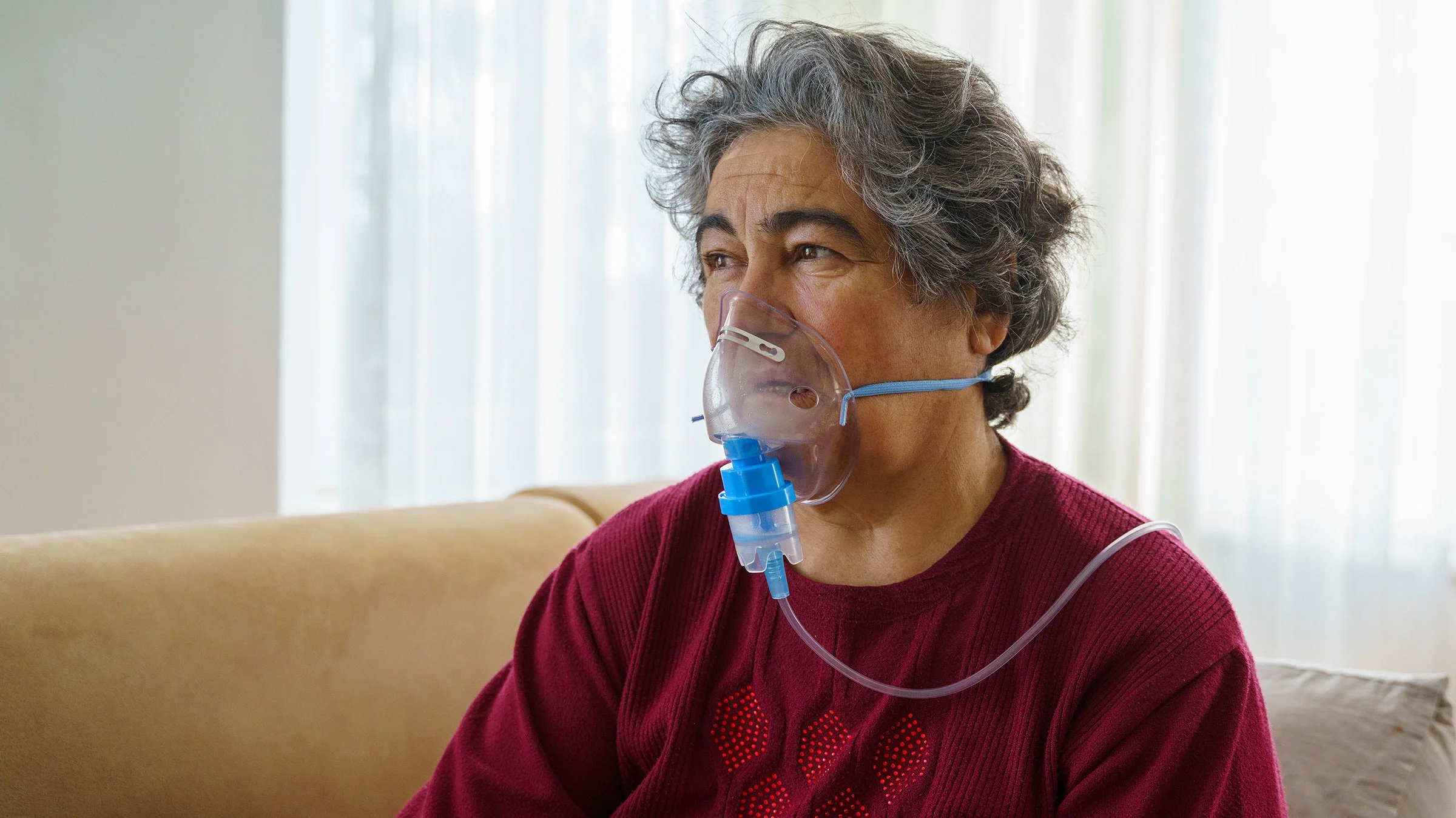 An older adult is doing inhalation therapy through an oxygen mask at home.