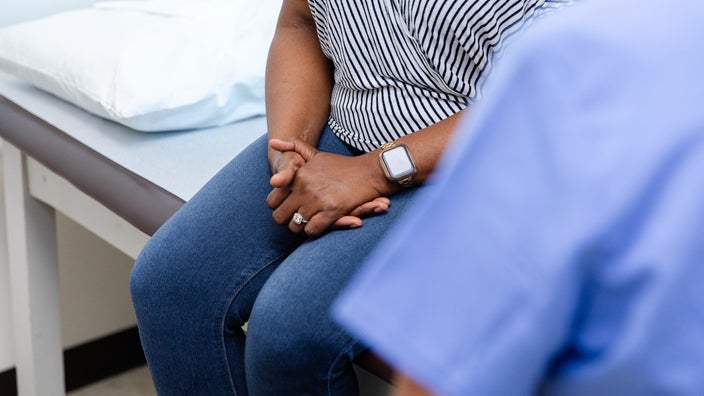 A woman sits on an examination table during a healthcare appointment.