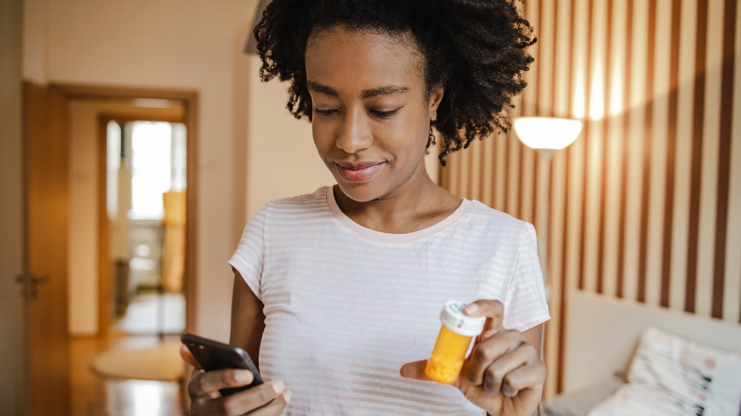 A person holding a pill bottle and smartphone.