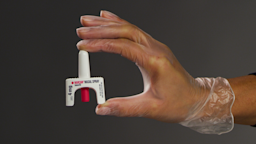 A person wearing a plastic glove holds Narcan nasal spray between their thumb and forefinger. 
Courtesy of Emergent
