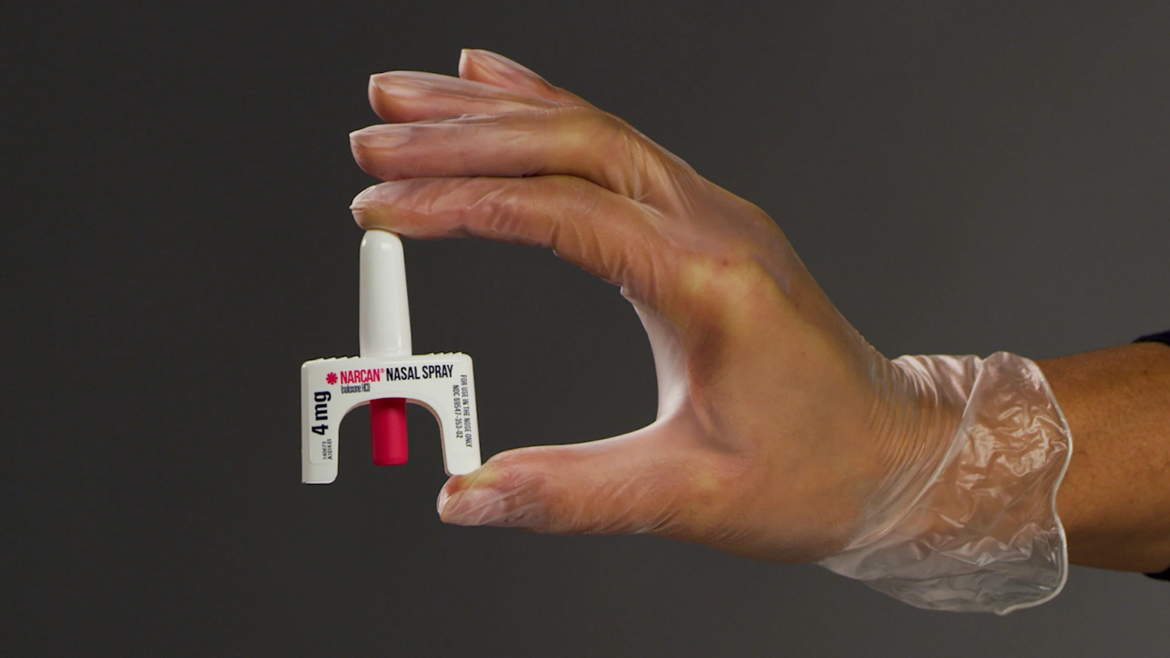 A person wearing a plastic glove holds Narcan nasal spray between their thumb and forefinger. 