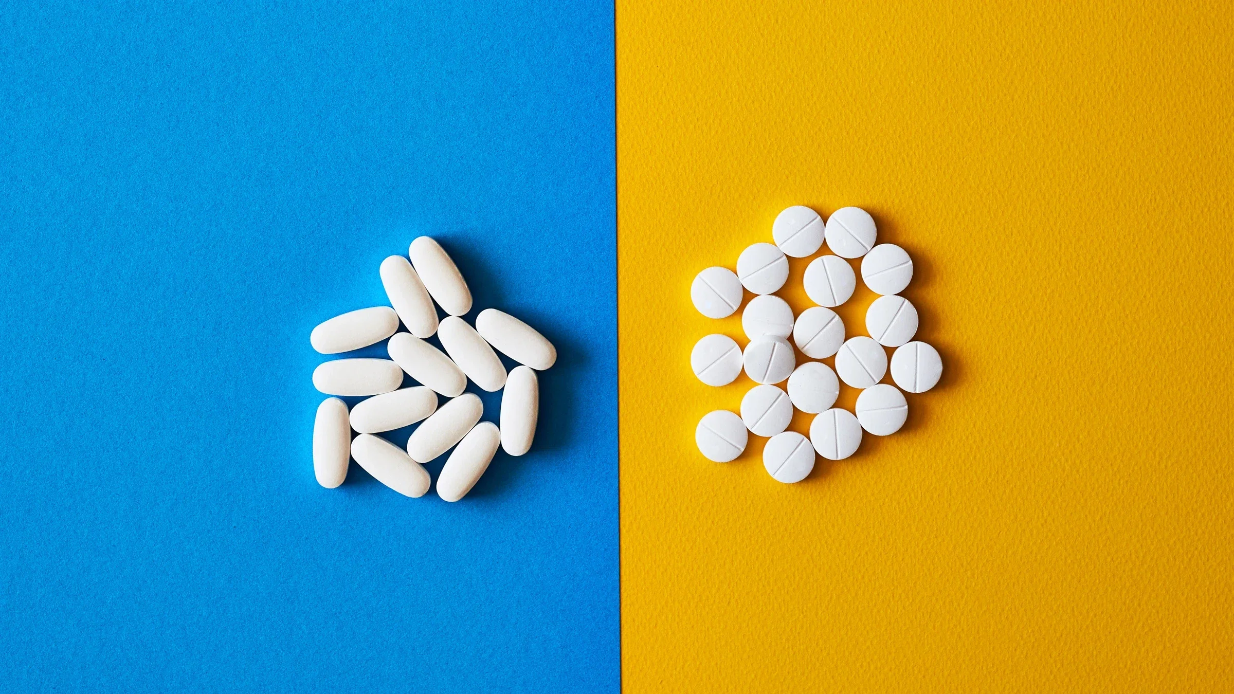 Two piles of pills next to each other, juxtaposed on a split blue/yellow background.
Hiraman/iStock via Getty Images 