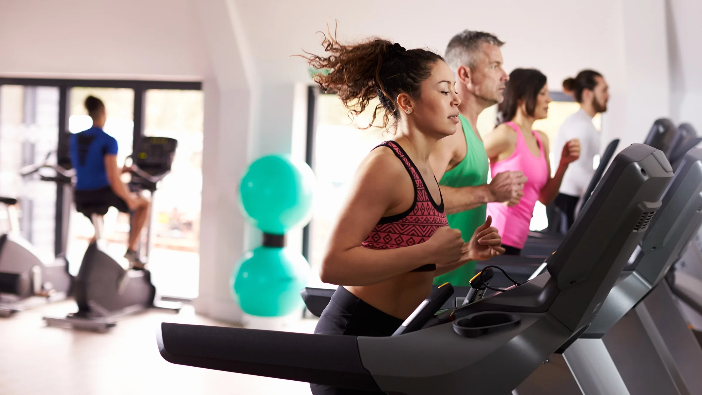 People at the gym using the treadmill and exercise bike.