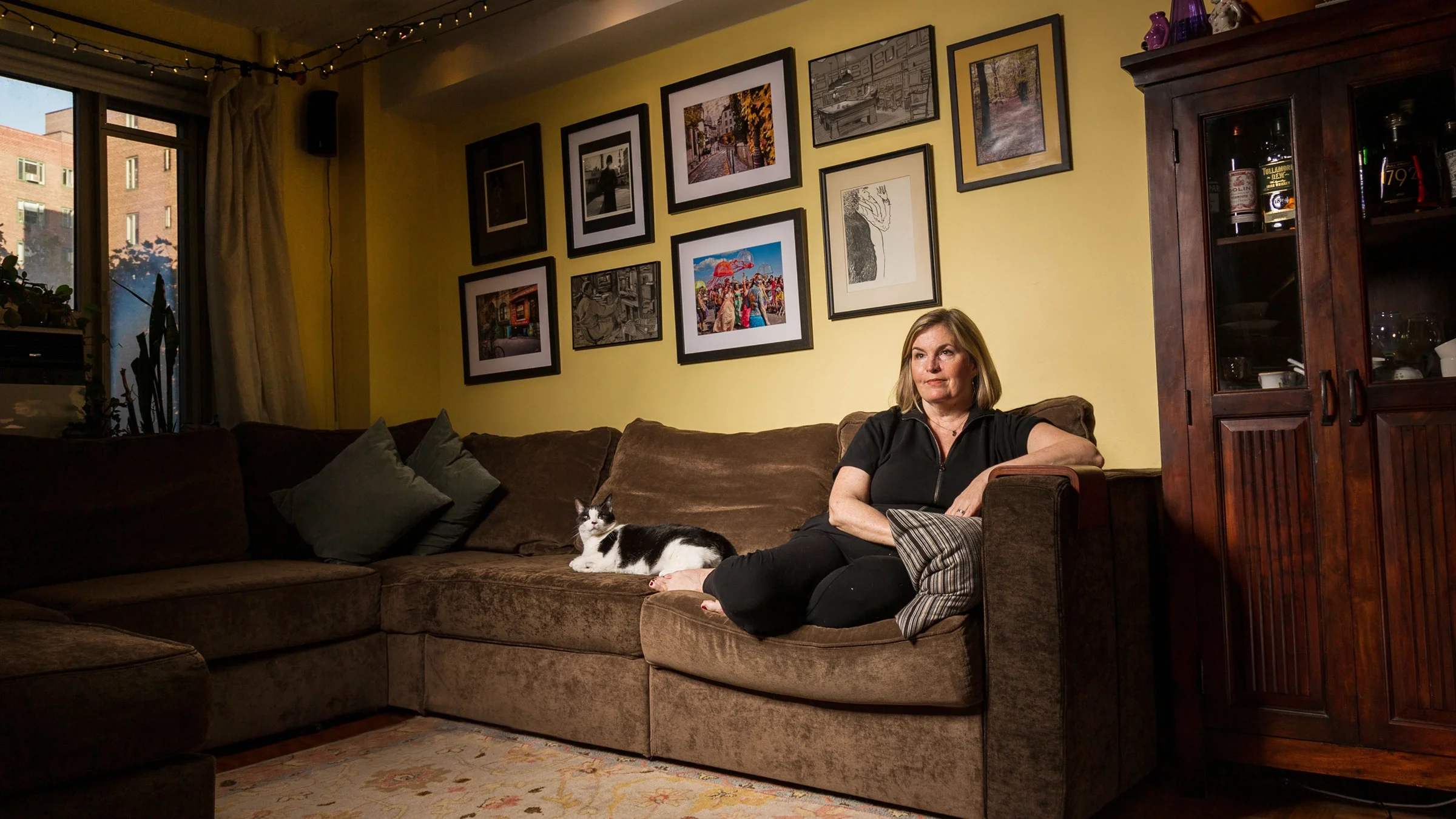 Portrait of Leigh Anne O’Connor at home on her couch. Her black-and-white cat is sitting next to her.