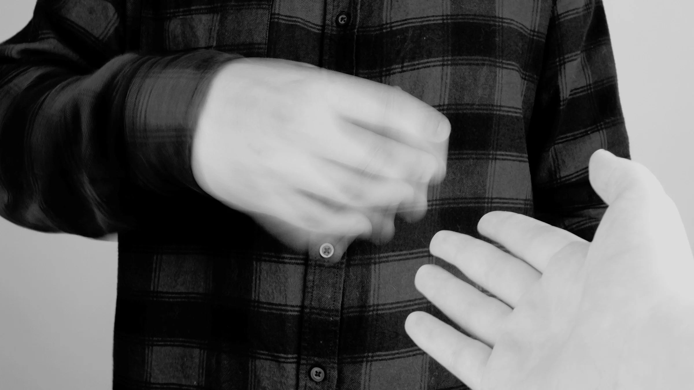 Black and white close-up of a person with hand tremors. It is visible in the frame by a blurry looking hand in motion.