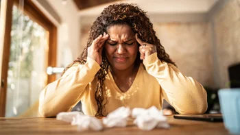 COVID-19: Headaches: woman with curly hair headache at home 1331824647