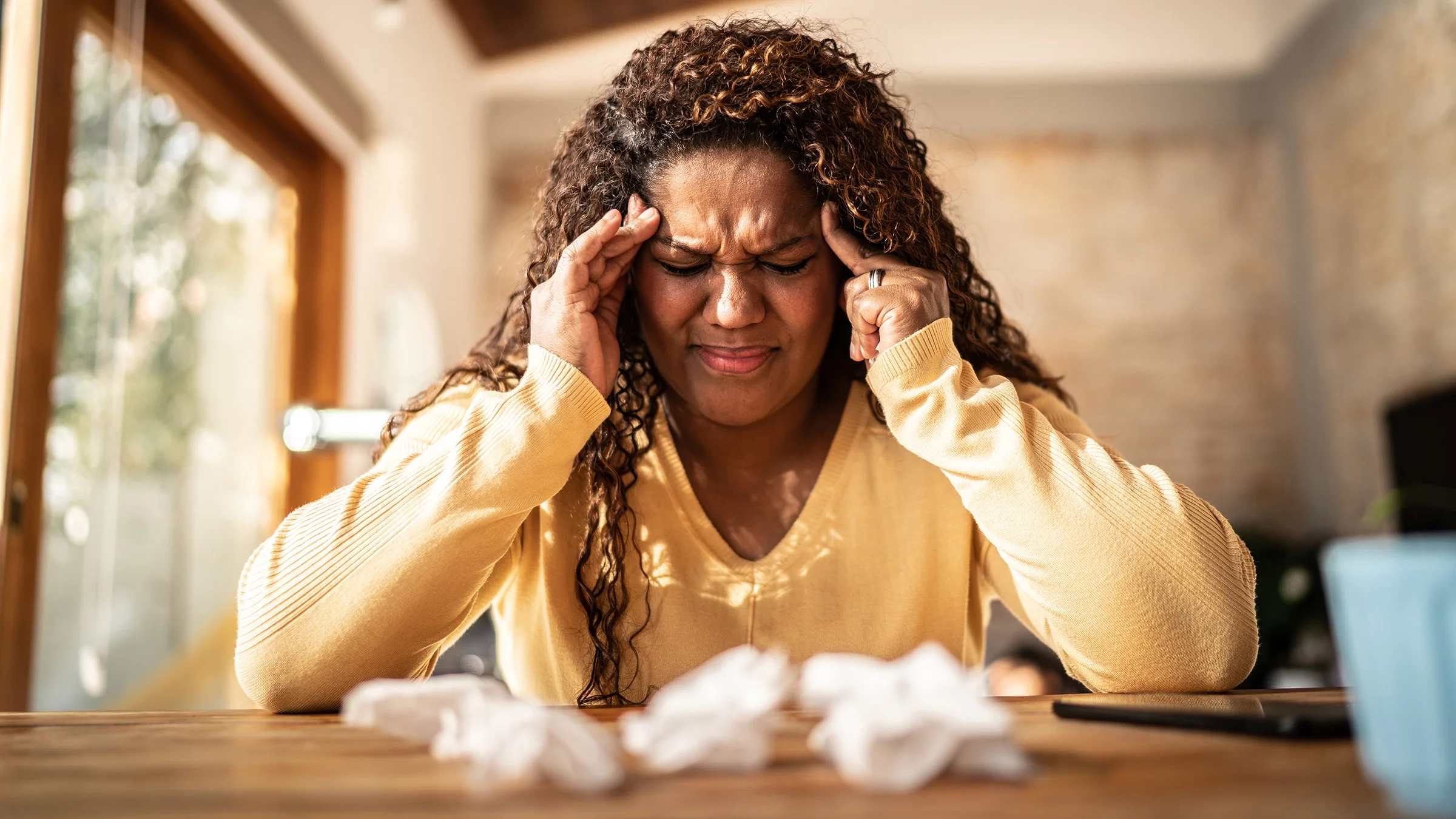 A woman with curly hair is experiencing a severe headache at home.