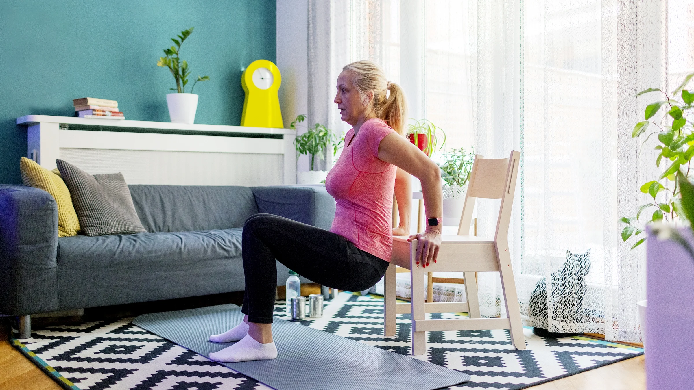 A woman leans on a chair and does a tricep dip.