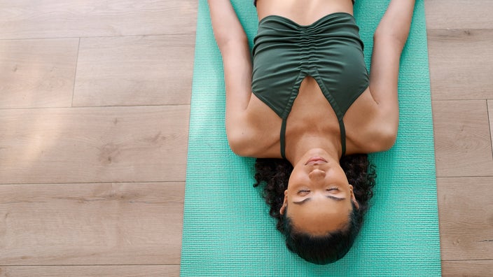Woman lies in shavasana yoga pose on a green yoga mat