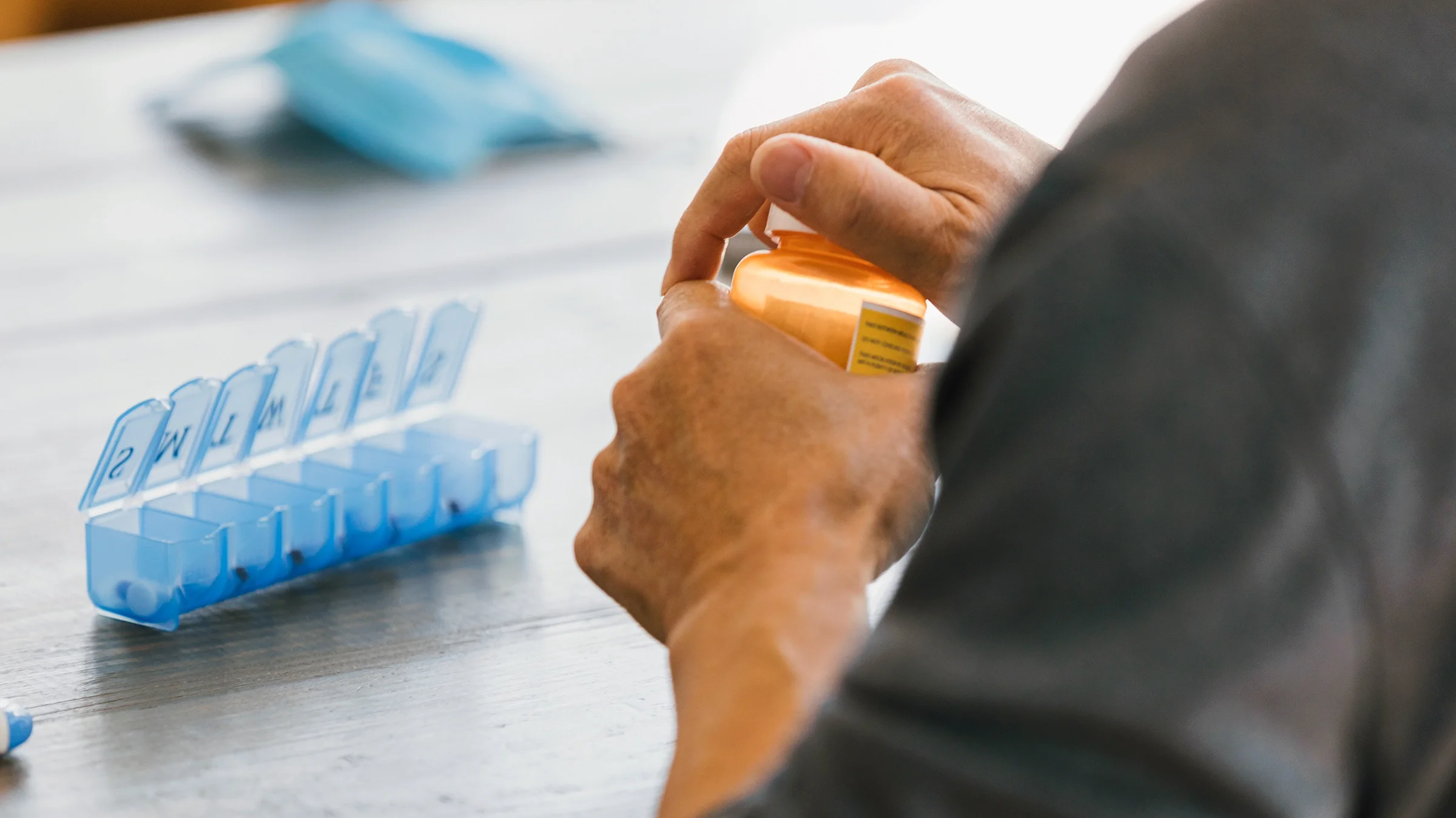 An older man removes a childproof cap from a bottle of medication.