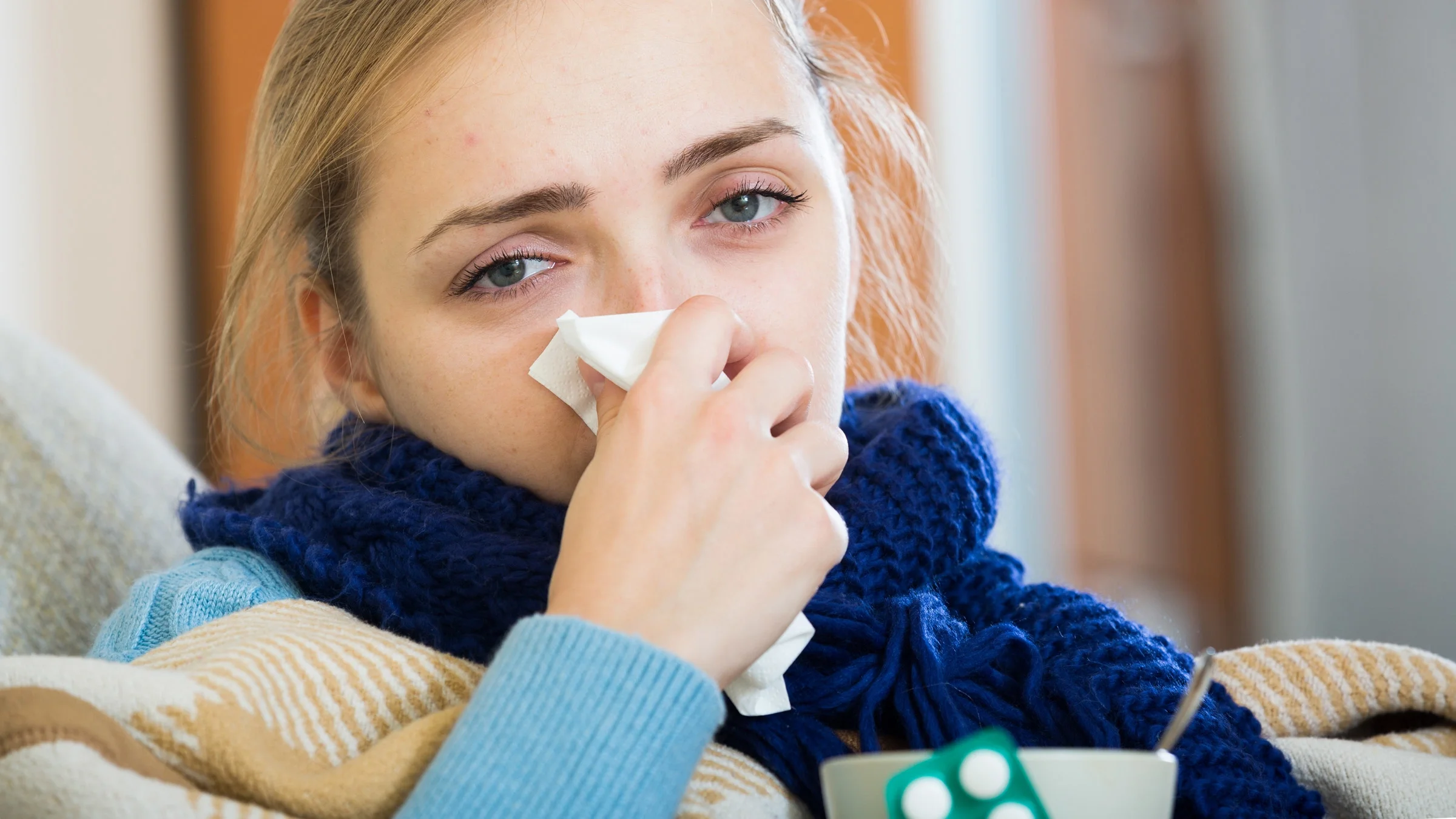 A person blowing their nose and holding a blister pack.