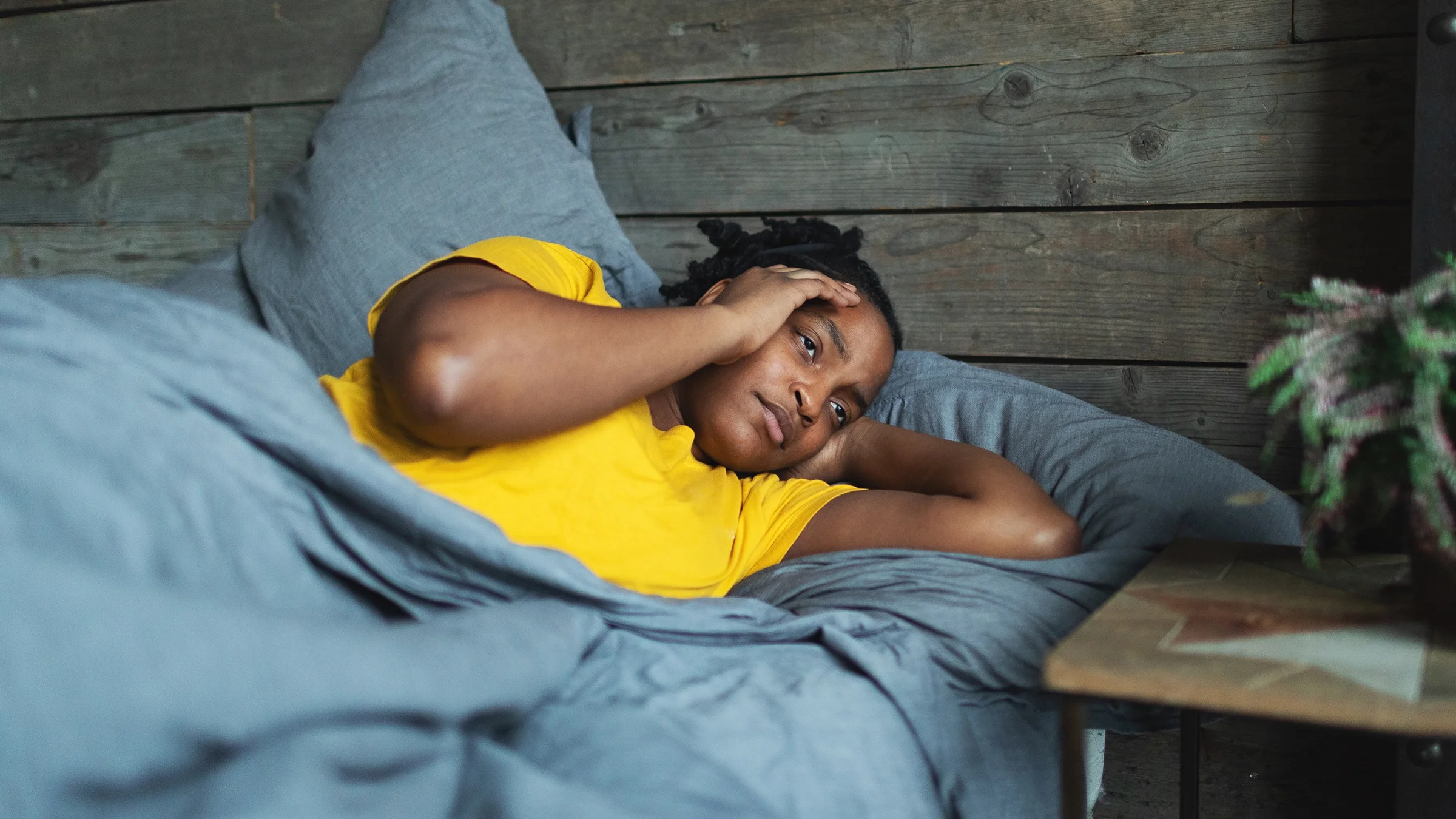 A woman lying in bed clutches her head in pain from a migraine.