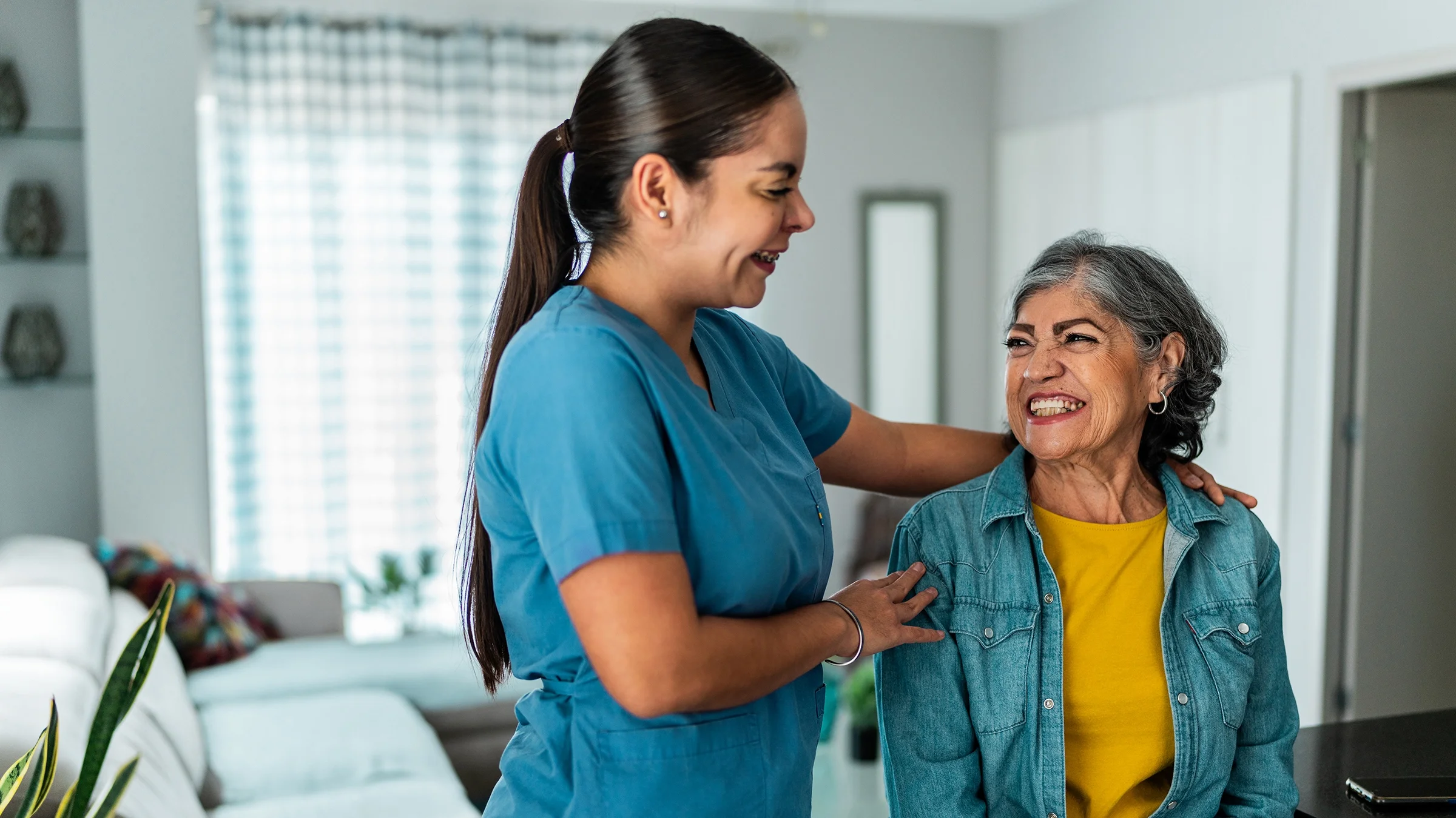 A home caregiver talks to an older woman at home.