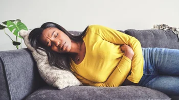 food-poisoning: stomach: pain: woman holding stomach laying down on couch-1355220254