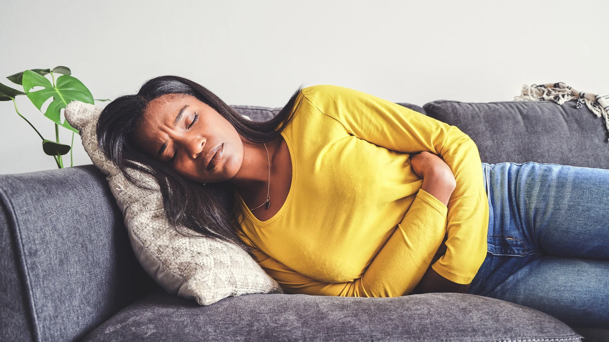 A woman is clutching her stomach while lying on the couch.
Moyo Studio/E+ via Getty Image