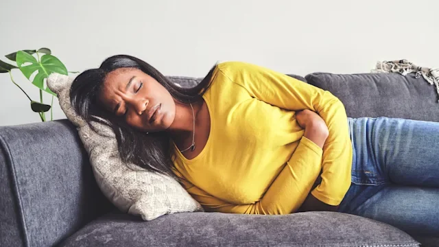 food-poisoning: stomach: pain: woman holding stomach laying down on couch-1355220254