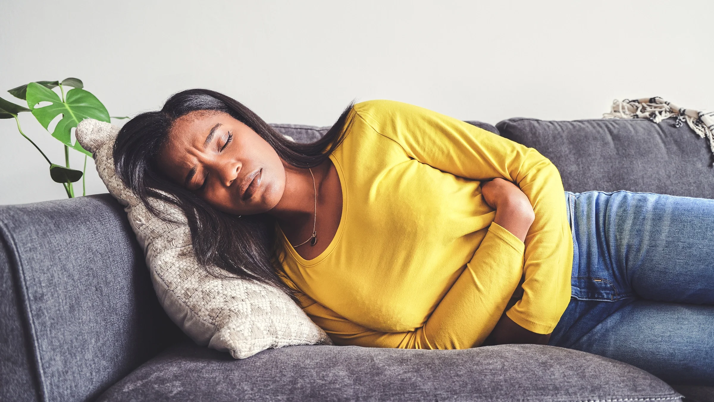 A woman is clutching her stomach while lying on the couch.