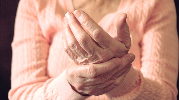 Close-up on a senior woman rubbing her hands. She is wearing a peach colored sweater.