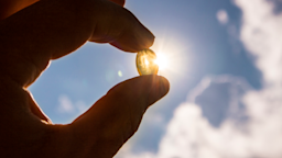 Person holding a vitamin D pill in between their fingers and up to the sunlight.
Helin Loik-Tomson/iStock via Getty Images