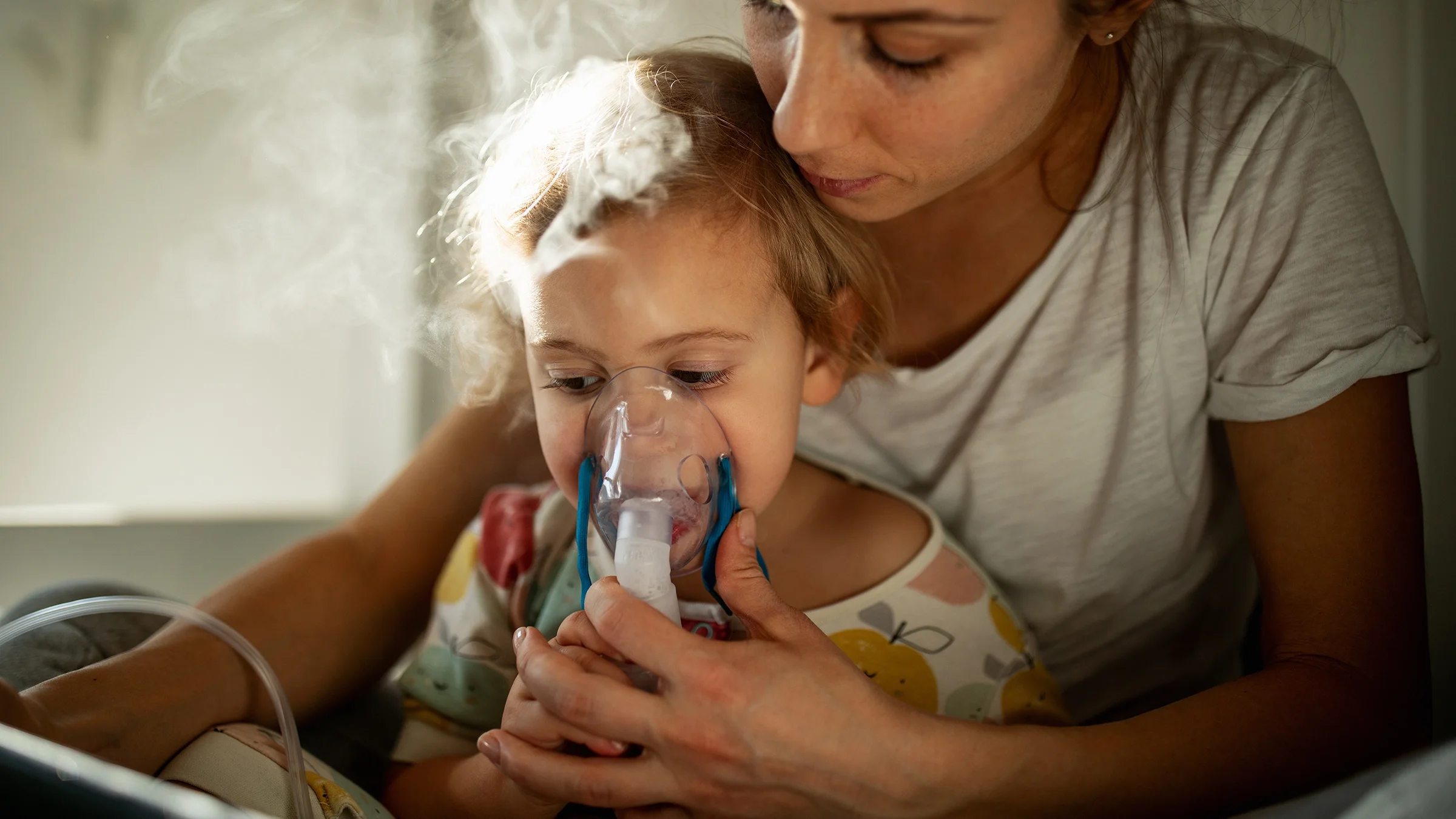 Mother helping young daughter with nebulizer treatment.