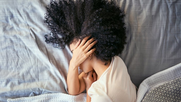 A person in ben on their side, covering their face. 