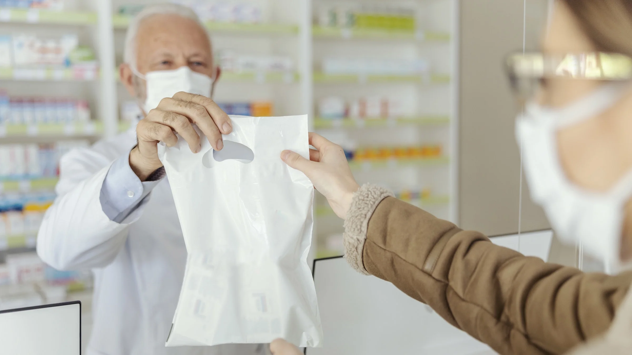 A pharmacist handing a prescription bag to a patient.