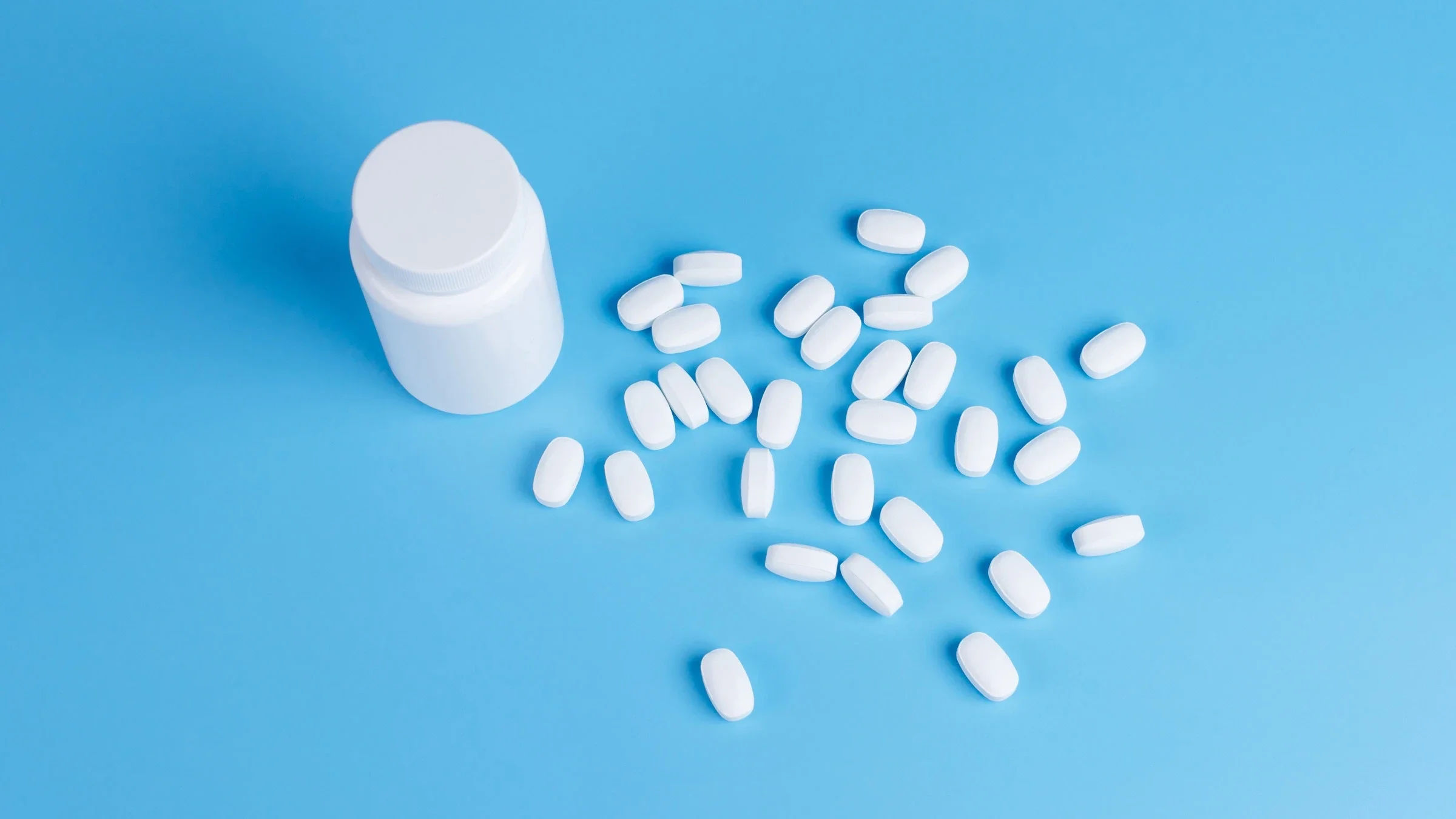 Pill bottle and pills on a blue background.