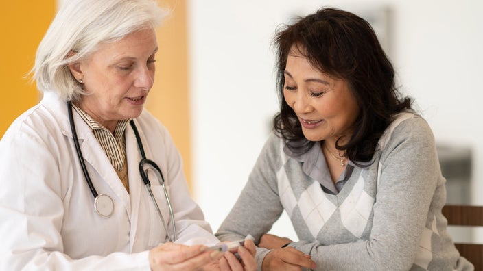A medical professional holds an injection pen while talking to her patient.