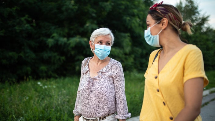 A masked parent and adult child taking a stroll outside and talking.