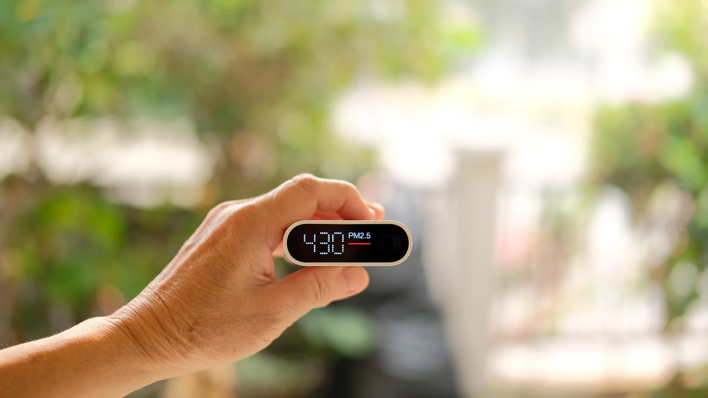 A home air quality monitor is shown in a person’s hand.
