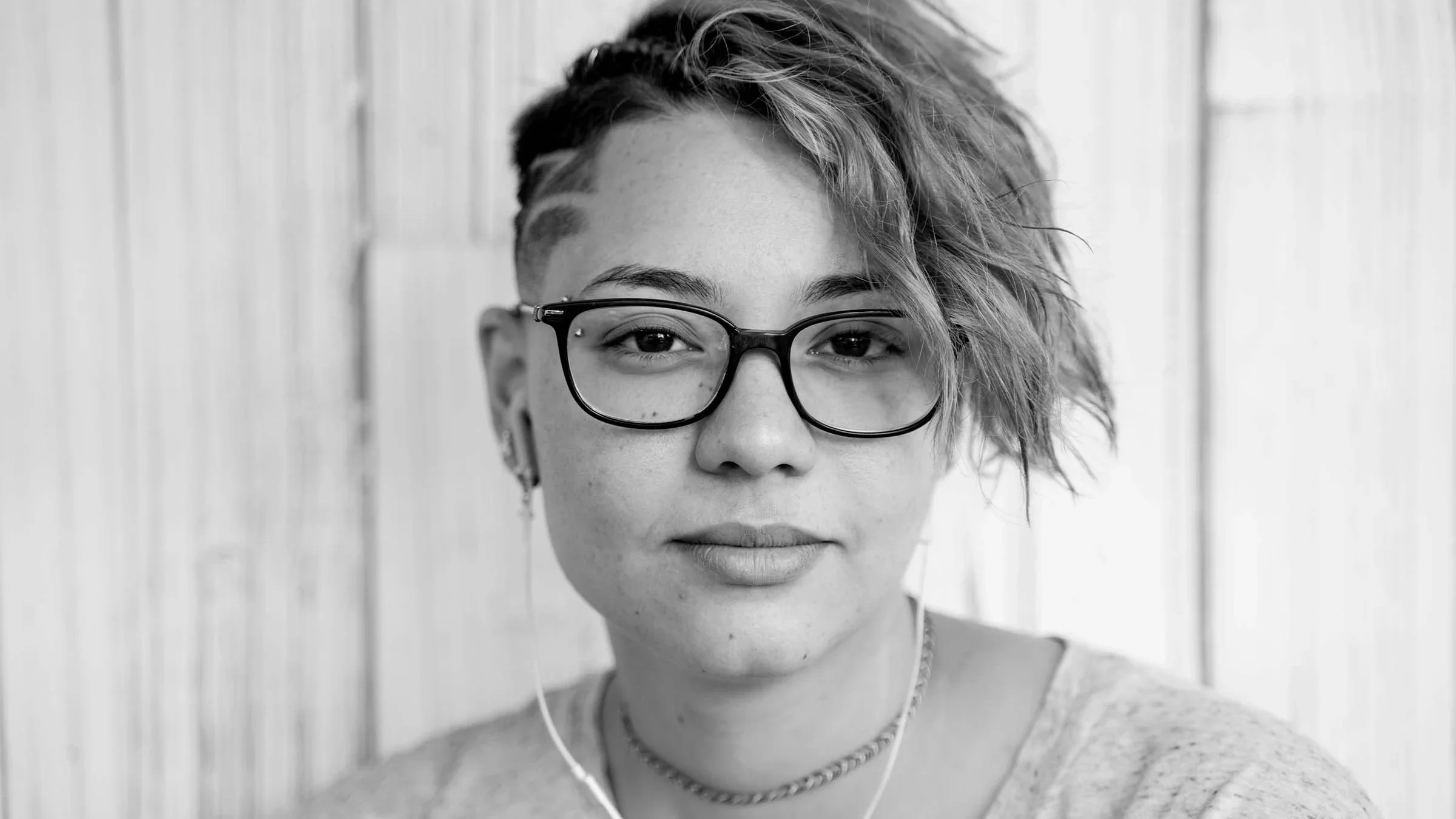 Black and white portrait of a young woman with glasses. She is wearing headphones and smiling softly.
Beaver/iStock via Getty Images