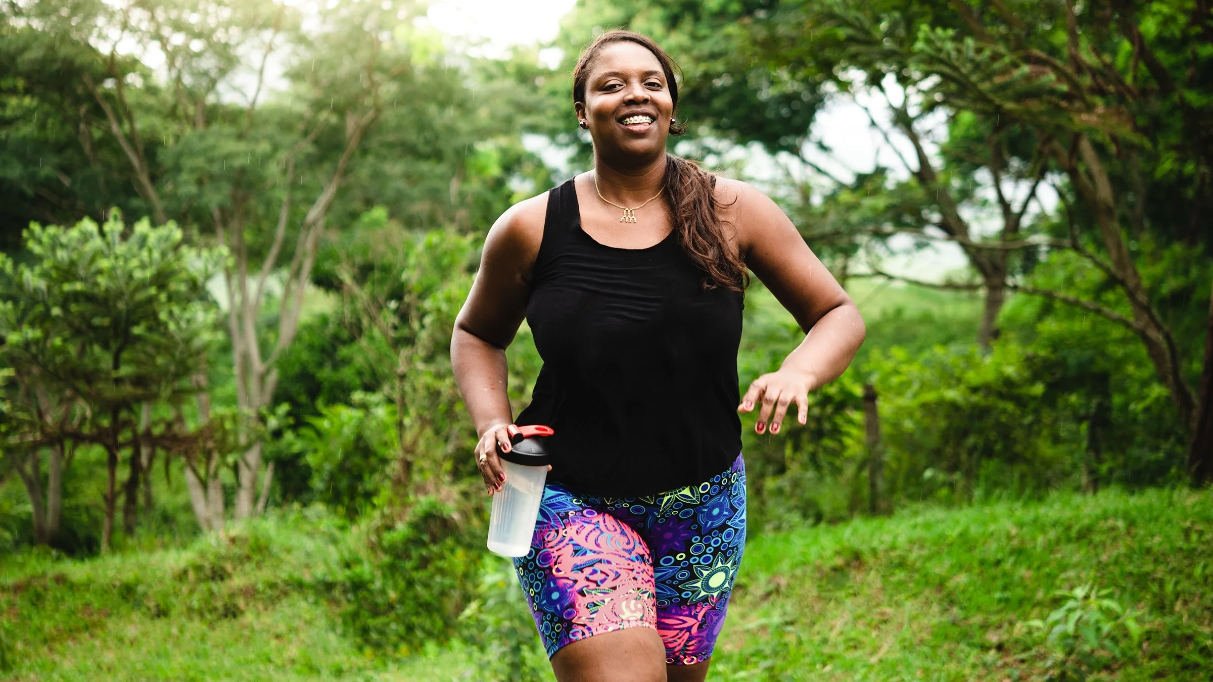 Young Black woman on a run through the trails. The trees are lusciously green all around her.