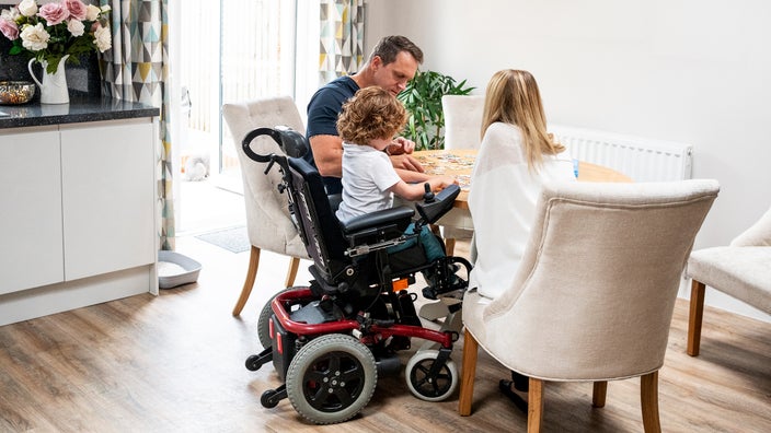 A boy in a wheelchair does a jigsaw puzzle with his parents. People with muscular dystrophy can experience trouble walking. The two most well-known types of muscular dystrophy are Duchenne and Becker.